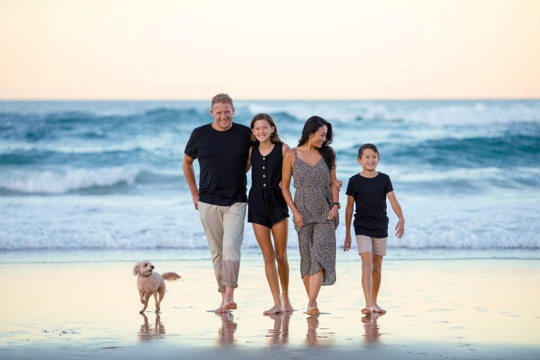Familie mit Hund spaziert am Strand entlang, Wellen im Hintergrund.