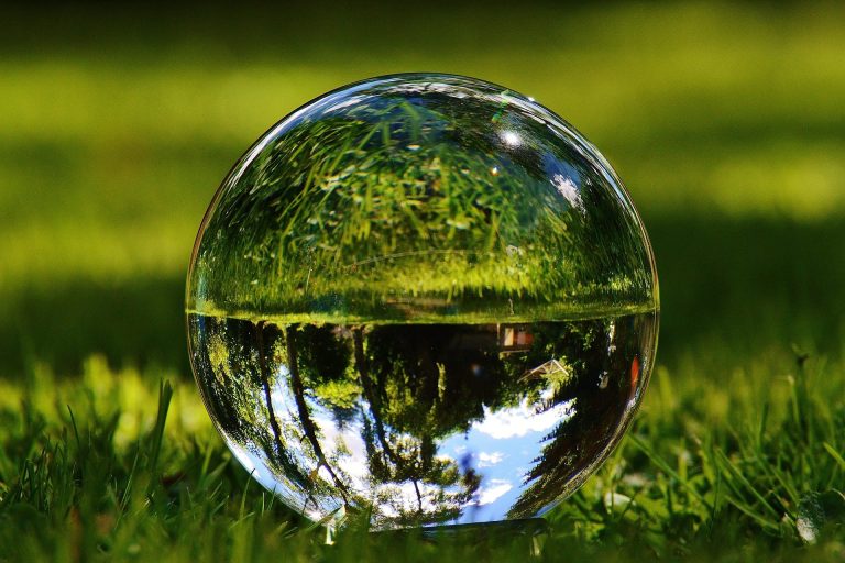 Glaskugel auf grünem Gras mit Reflexion von Bäumen und Himmel.