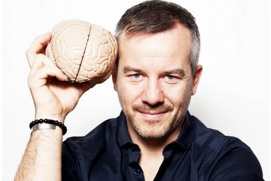 Markus Hoffmann hält ein Gehirnmodell oder Basketball-ähnliche Mütze an seinem Kopf und lächelt.
